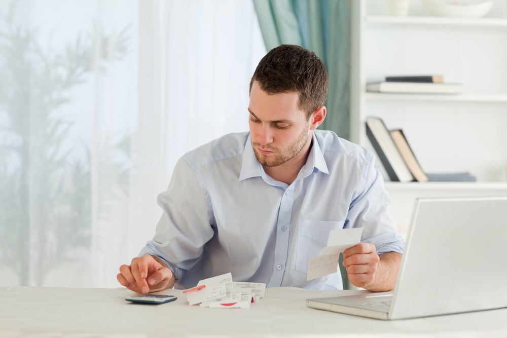 Young businessman in need of debt support calculating bills from receipts