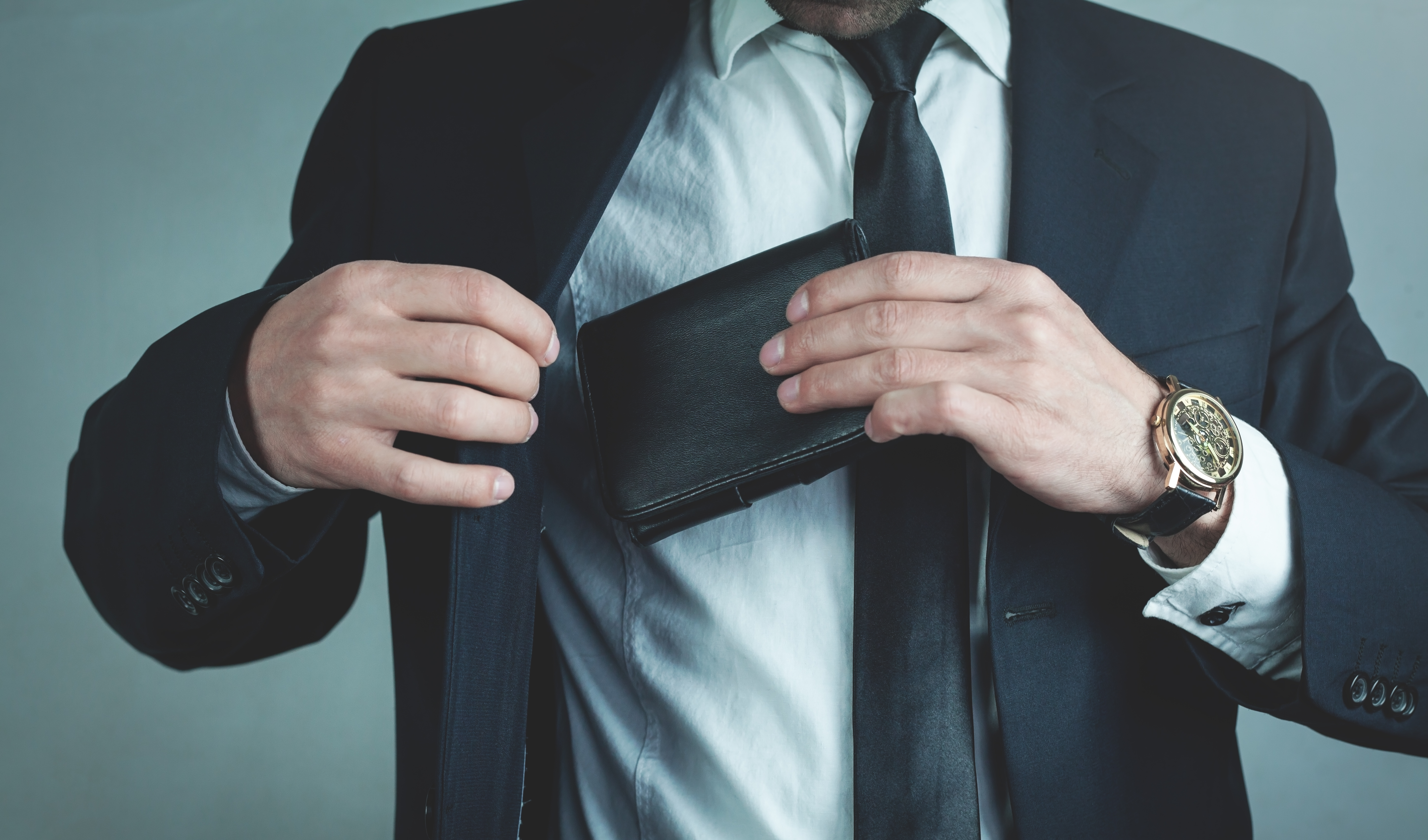 Businessman pulls his leather wallet into suit pocket, representing S455 tax on liquidation